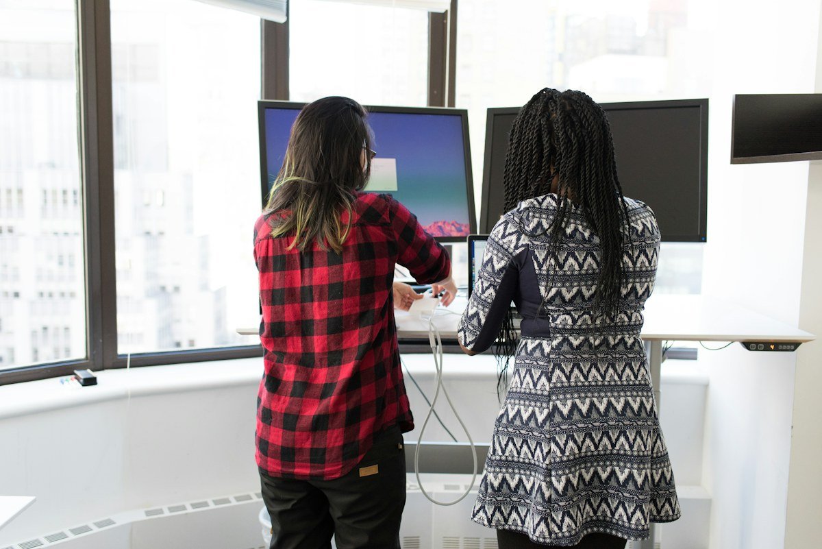 Two women discussing work beside computer monitors